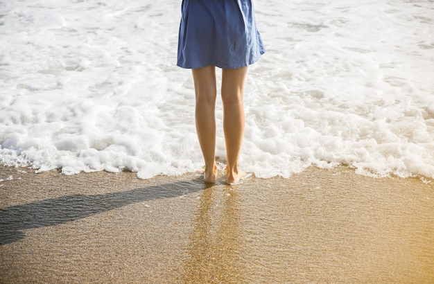 Beautiful girl in blue dress is walking on the beach Amazing summer photo Woman near the sea Holiday travel concept Slim legs Warm ocean water