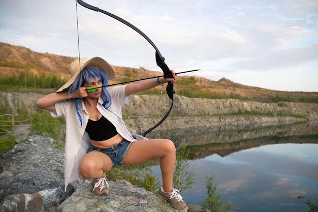 a beautiful girl in a blue wig and a straw hat with a bow and arrow in her hands