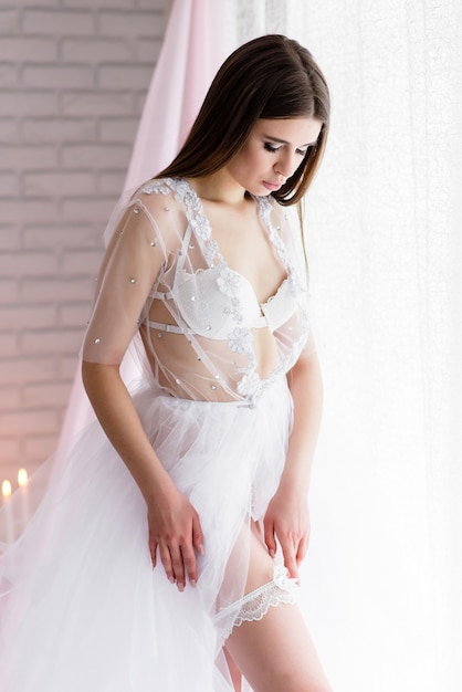 Photo beautiful girl bride in a white lace boudoir dress linen closed with a veil on the wedding day morning on the beautiful scenery of flowers.