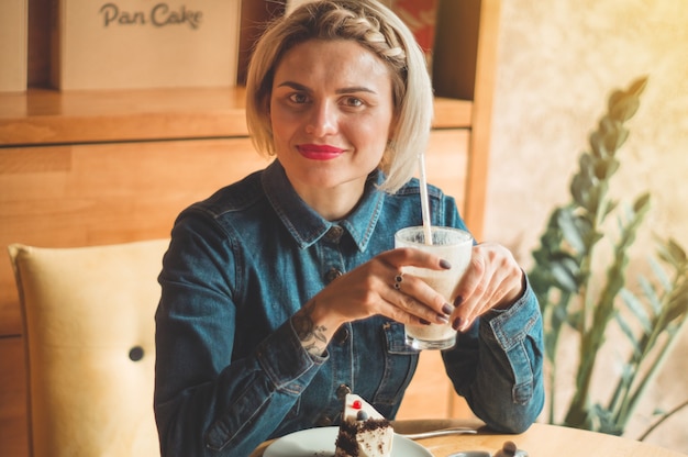 Beautiful girl in a cafe enjoying a cold cocktail. Hipster girl holding summer cocktail. Refreshment drink in sunny day