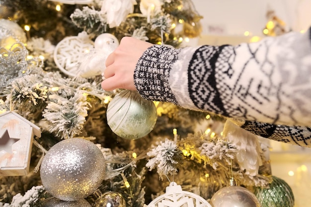 Beautiful girl in a Christmas sweater closeup hangs a Christmas ball on a Christmas tree Preparing for the celebration of the new year christmas