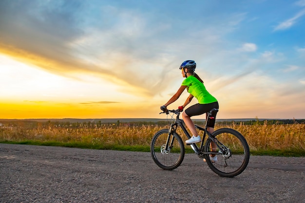 Photo beautiful girl cyclist riding a bike on the road towards the sunset