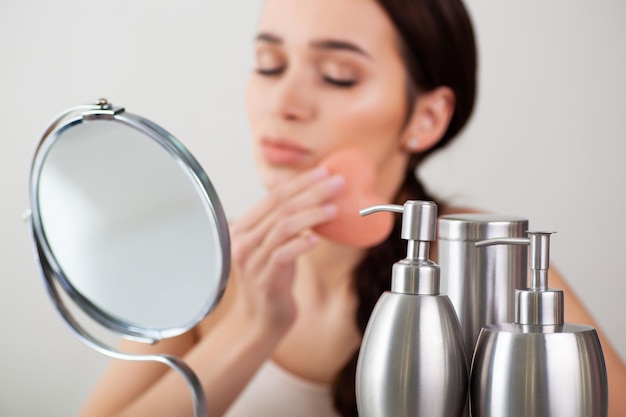 Beautiful girl doing makeup with a heartshaped sponge in front of a mirror