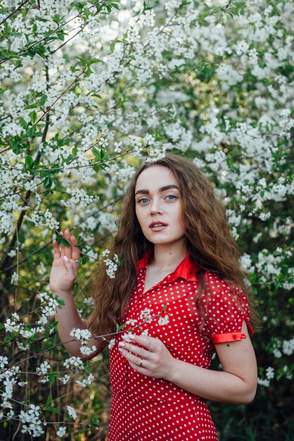 A beautiful girl in a dress stands next to a blooming cherry bus