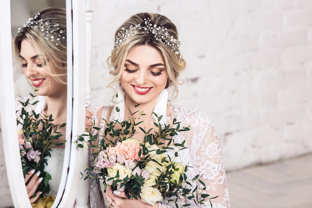 Beautiful girl dressed in peignoir and underwear sits on floor near mirror and holds bouquet in her hands