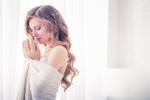 Beautiful girl drinking coffee by the window in the morning.