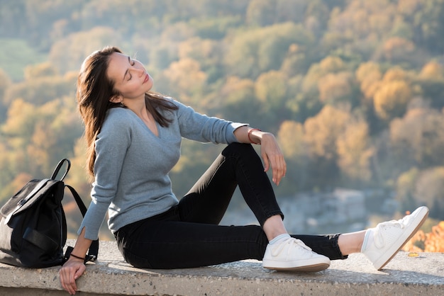 Beautiful girl enjoys nature sitting on a hill with closed eyes. Sunny day