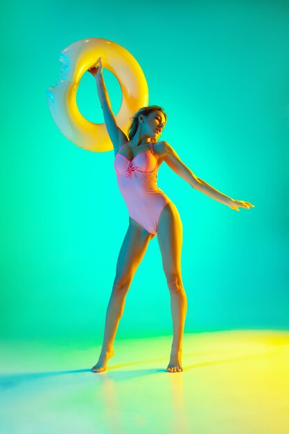 Beautiful girl in fashionable swimsuit isolated on gradient studio background in neon light.