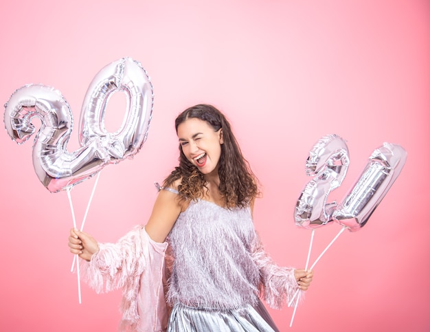 A beautiful girl in a festive mood dancing on a pink  wall and holds in her hands silver balloons for the new year concept