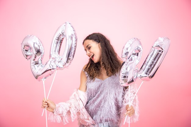 Beautiful girl in a festive mood poses on a pink  wall and holds silver balloons for the new year concept