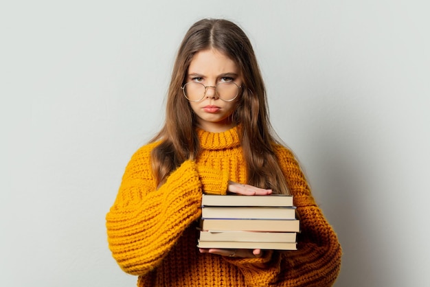 Beautiful girl in glasses and yellow sweater with books on white background