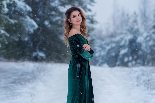 Beautiful girl in a green long dress in a snowy forest