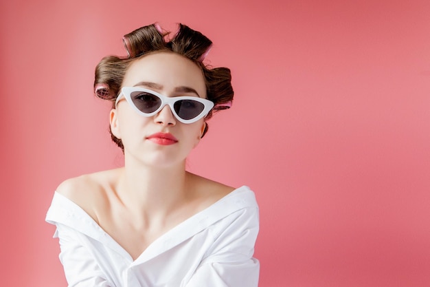 Beautiful girl in hair curlers on pink background