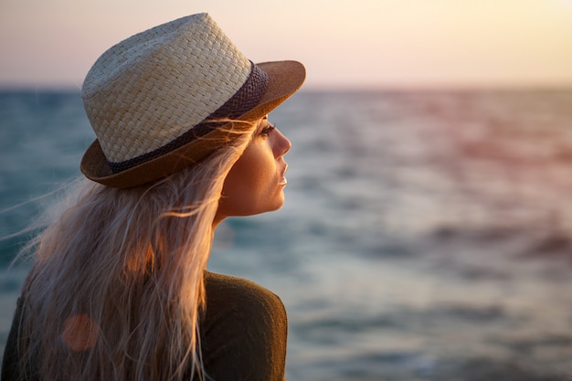 Beautiful girl in hat by the sea at sunset.