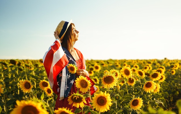 Beautiful girl in hat with the American flag in a sunflower field 4th of July Fourth of July Freedom