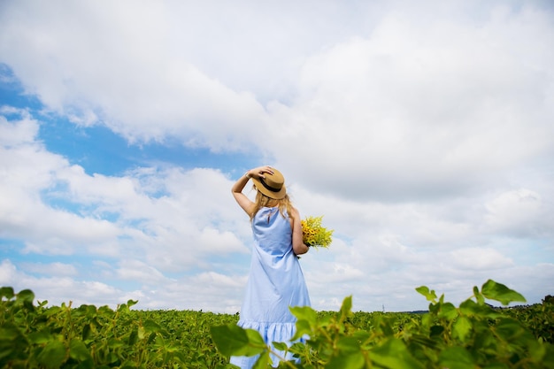 Beautiful girl in a hat with a bouquet of flowers chic green field