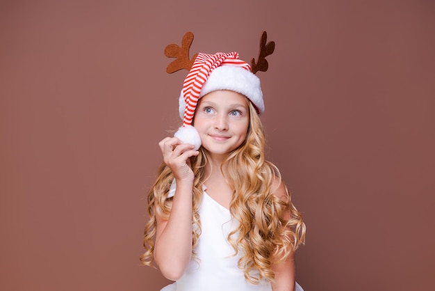 Beautiful girl in hat with deer antlers and in white dress smiles cutely