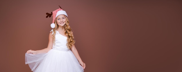 Beautiful girl in hat with deer antlers and in white dress smiles cutely