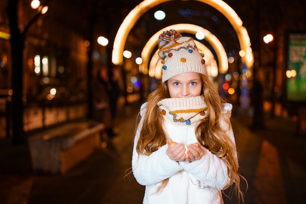 Beautiful girl holding a garland in her hand in the evening on the street in winter