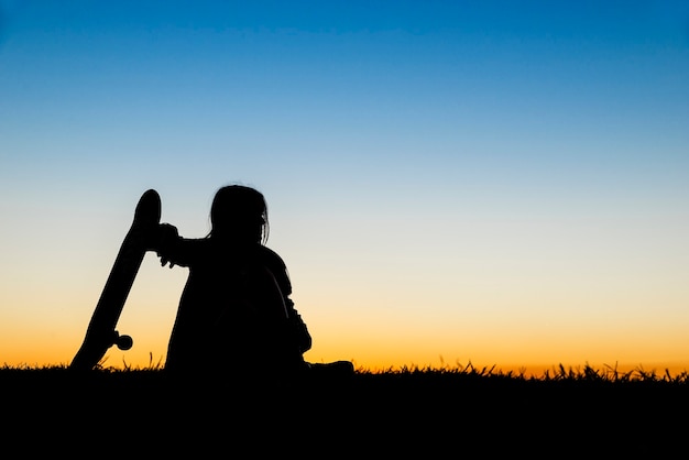 Beautiful girl holding a skateboard with the sunset in the background. Backlight