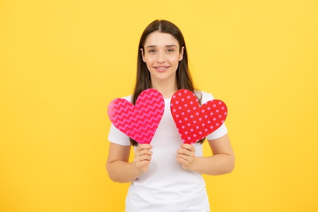 Beautiful girl holding valentines gift on yellow background Portrait of young woman holding red paper heart