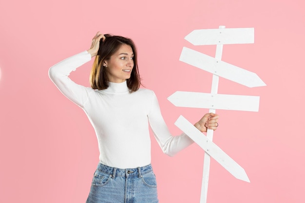 Beautiful girl holding white road signs in her hand isolated on pink background