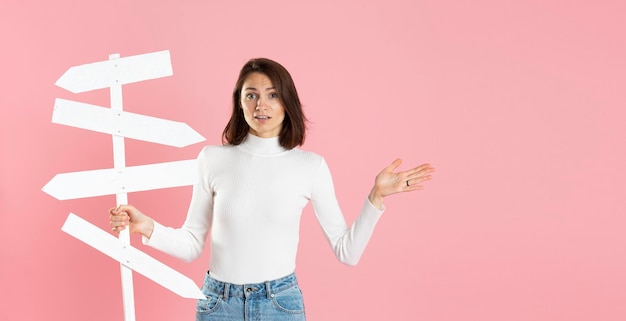 Beautiful girl holding white road signs in her hand isolated on pink background