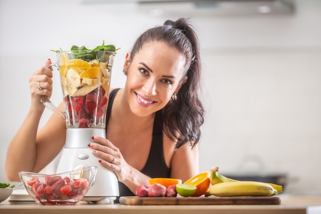 Beautiful girl holds blender full of healthy stuff before mixing it into a healthy breakfast.