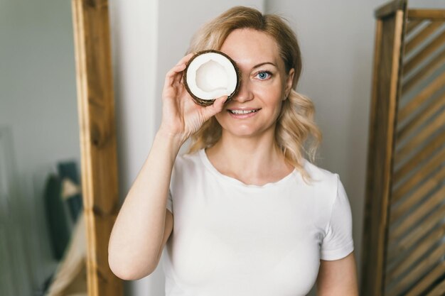 Photo a beautiful girl holds a half of a coconut and covers her eye