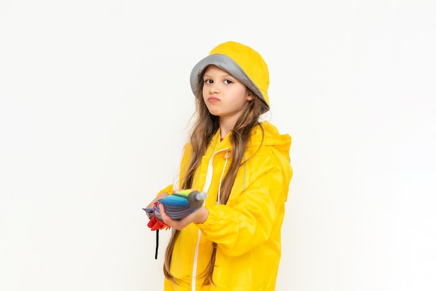 A beautiful girl holds a multicolored closed umbrella on a white isolated background A child dressed in a yellow raincoat and a panama hat from the rain Rainy weather concept