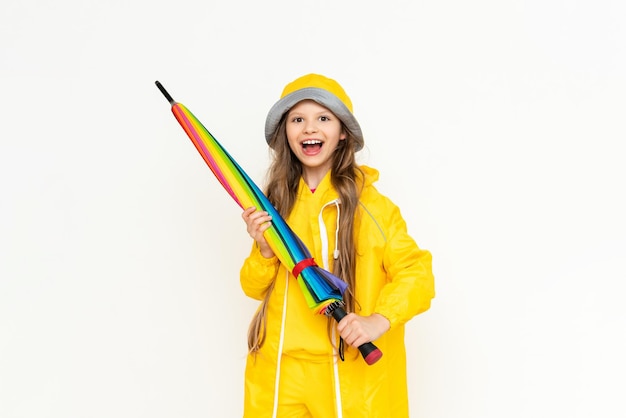 A beautiful girl holds a multicolored closed umbrella on a white isolated background A child dressed in a yellow raincoat and a panama hat from the rain