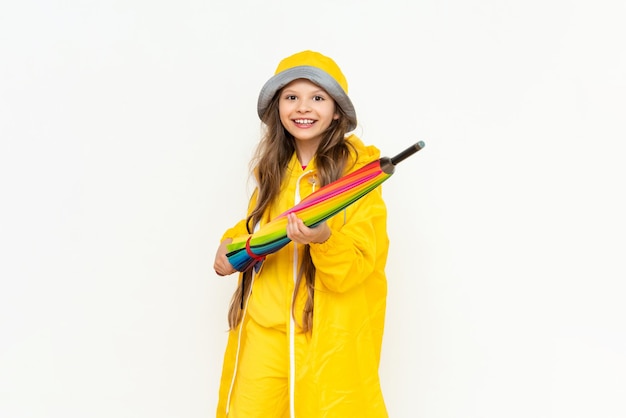 A beautiful girl holds a multicolored closed umbrella on a white isolated background A child dressed in a yellow raincoat and a panama hat from the rain