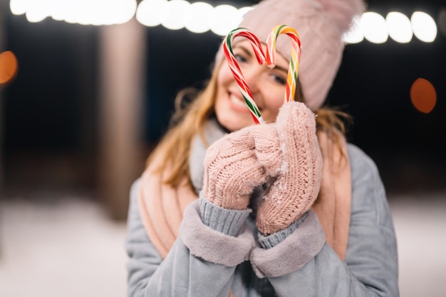 Beautiful girl holds sweet caramel canes in her hands Happy winter time in the forest