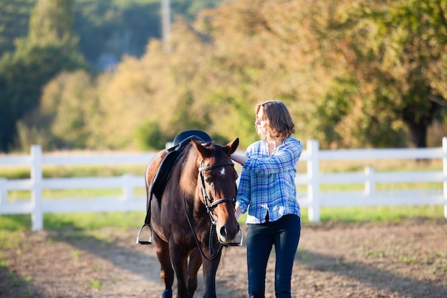 Beautiful girl leading her brown horse at the farm