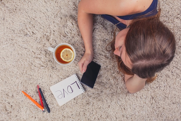 Beautiful girl lying on the carpet at home and reading sms