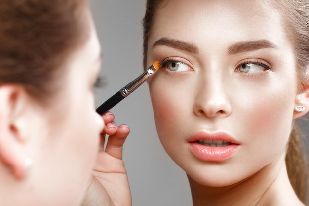 Beautiful girl makes herself a makeup in the mirror Beauty face Photo taken in studio