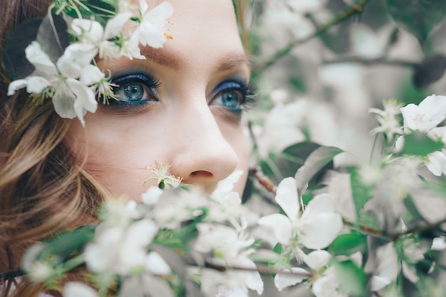 Beautiful girl model with bright makeup among white flowers. Portrait of a woman close-up