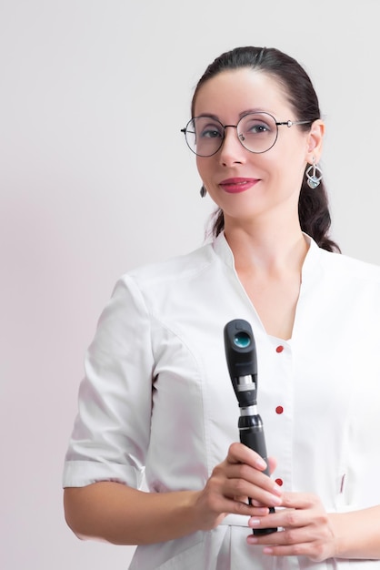 Beautiful girl optometrist doctor in a white coat with a retinoscope in her hand Reception in a modern ophthalmological clinic glasses shop