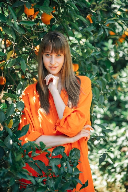 Beautiful girl in orange dress is looking at camera by putting hand under chin in orange garden