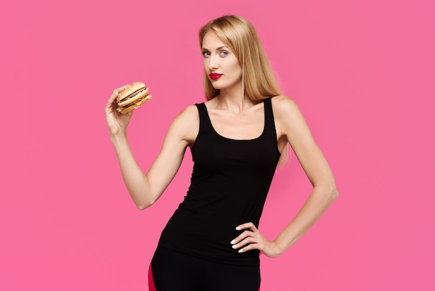 Beautiful girl on a pink background holds a burger The concept of an unhealthy diet