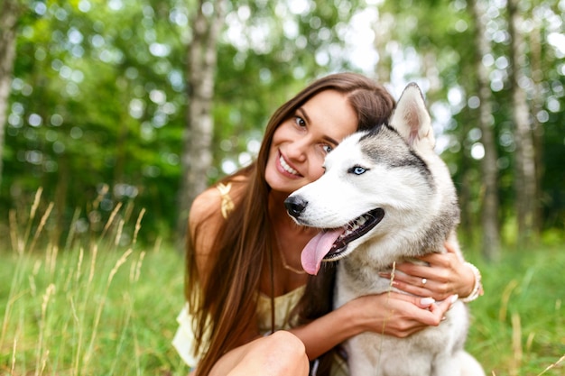 Beautiful girl plays with a dog black and white husky with blue eyes green field Siberian husky