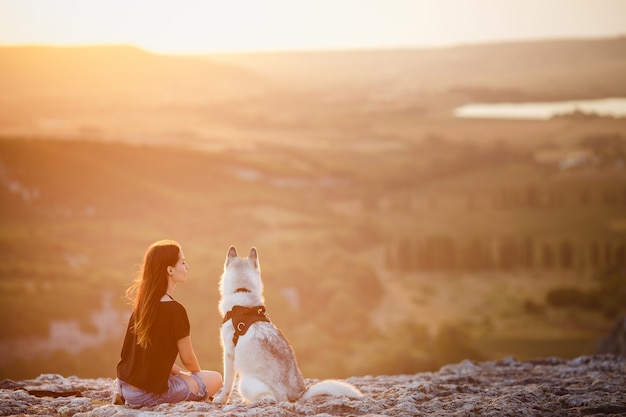 Beautiful girl plays with a dog, grey and white husky, in the mountains at sunset. Indian girl and her wolf