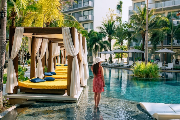 A beautiful girl poses on site near the pool, next to beds and sunbeds in the open air. The concept of tourism and leisure