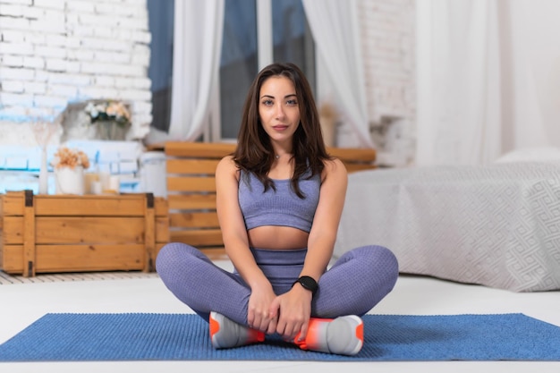 Beautiful girl in a purple tracksuit is doing fitness at home Fitness girl in a relaxed pose on a yoga mat Looks into the camera Fit girl leading an active lifestyle