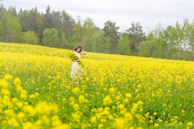 Beautiful girl in a rapeseed field. A child in a blooming field with yellow flowers. Plantation of yellow flowers