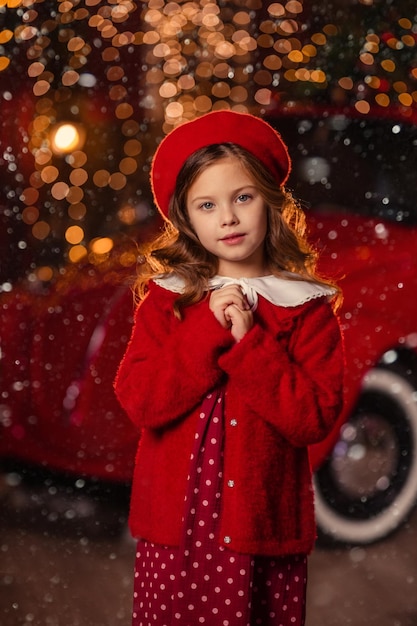 Beautiful girl in a red dress and beret on the background of Christmas lights and red retro car