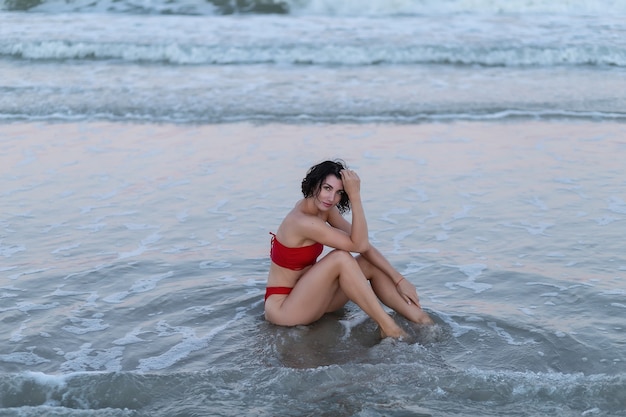 Beautiful girl in a red swimsuit sunbathes on a concrete pier against the background of the blue sea