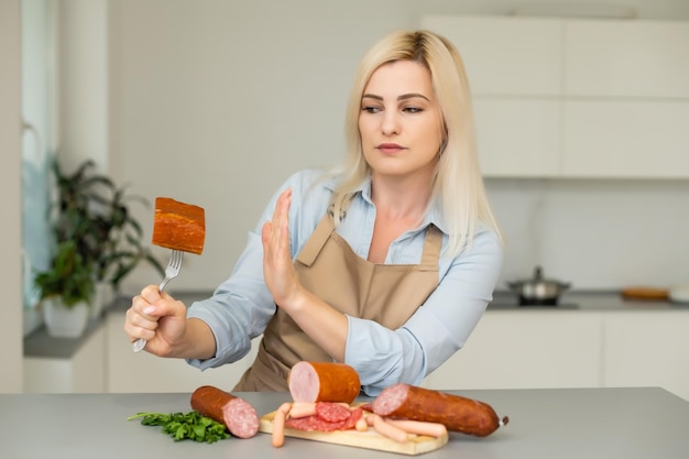 A beautiful girl refuses sausages on a neutral background. The concept of vegetarianism.