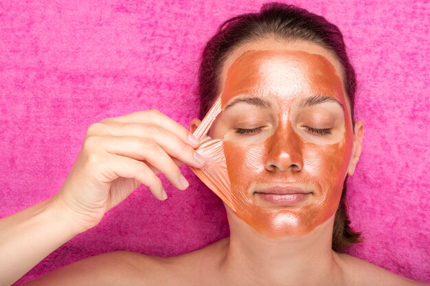 Beautiful girl removes a bronze color cosmetic mask from her face