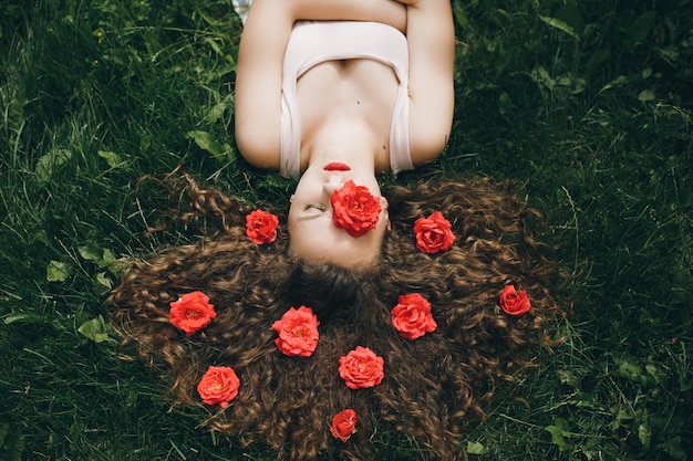 Beautiful girl rest at the green grass with red roses in her hair